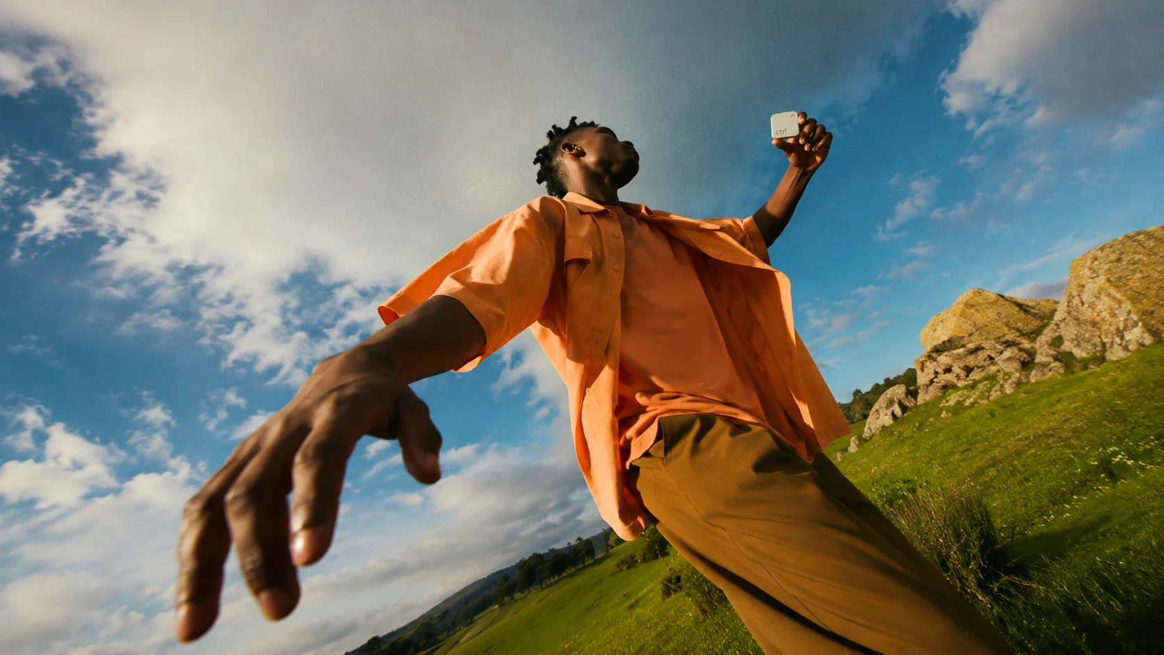 A man on a green meadow holding the ctrl key up against the summer sky