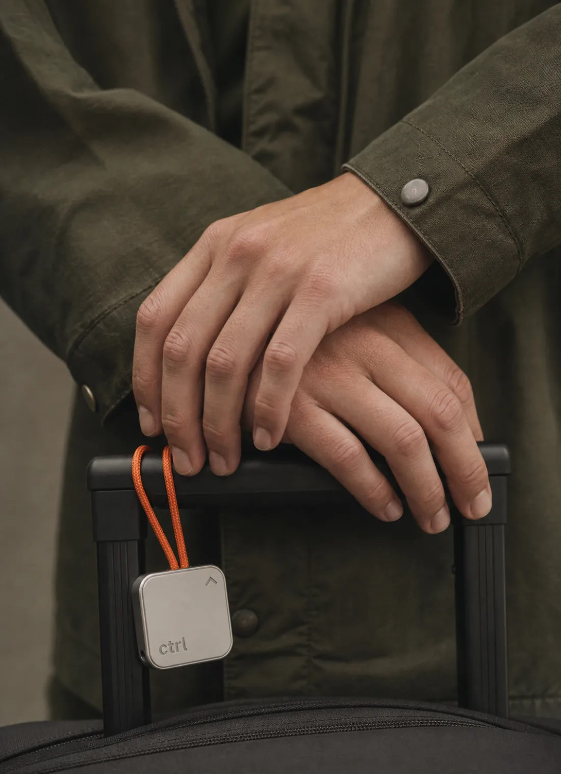 Hands crossed on a suitcase handle with the ctrl key hanging from a cord